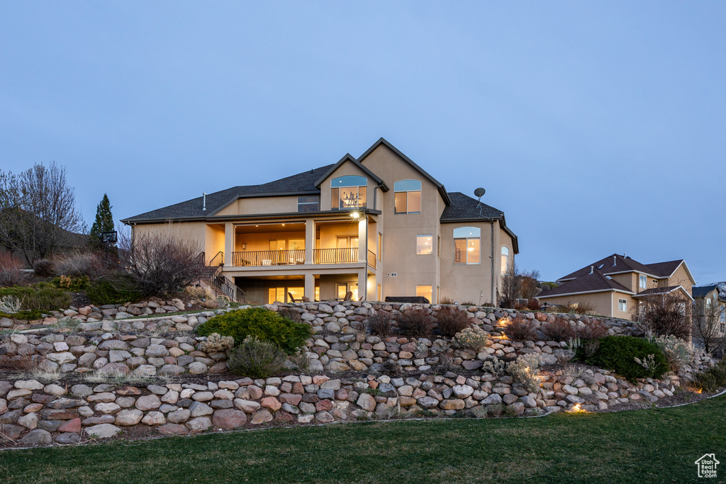 Back of house featuring a shingled roof, stucco siding, and a balcony