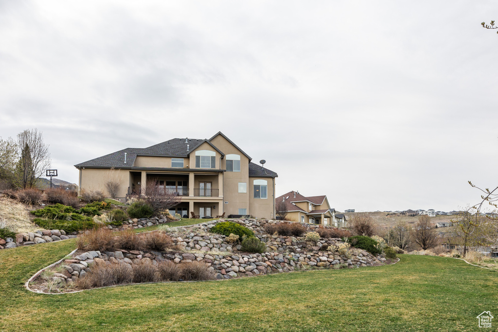 Rear view of property featuring a balcony, a lawn, and stucco siding