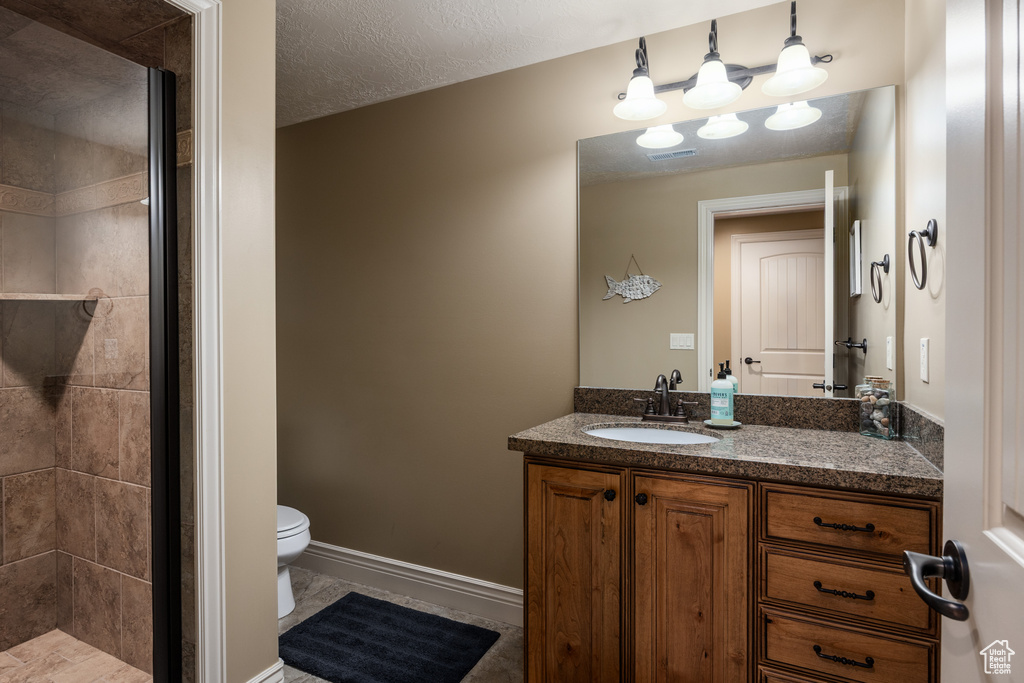Bathroom featuring vanity, toilet, baseboards, a textured ceiling, and a shower stall