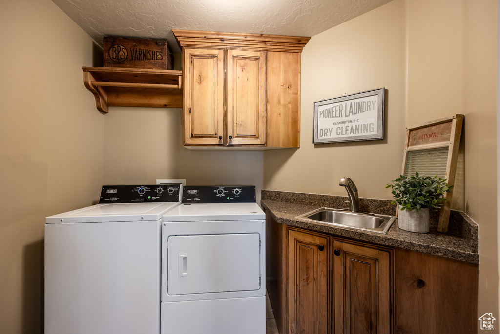 Clothes washing area featuring cabinet space, a textured ceiling, a sink, and independent washer and dryer