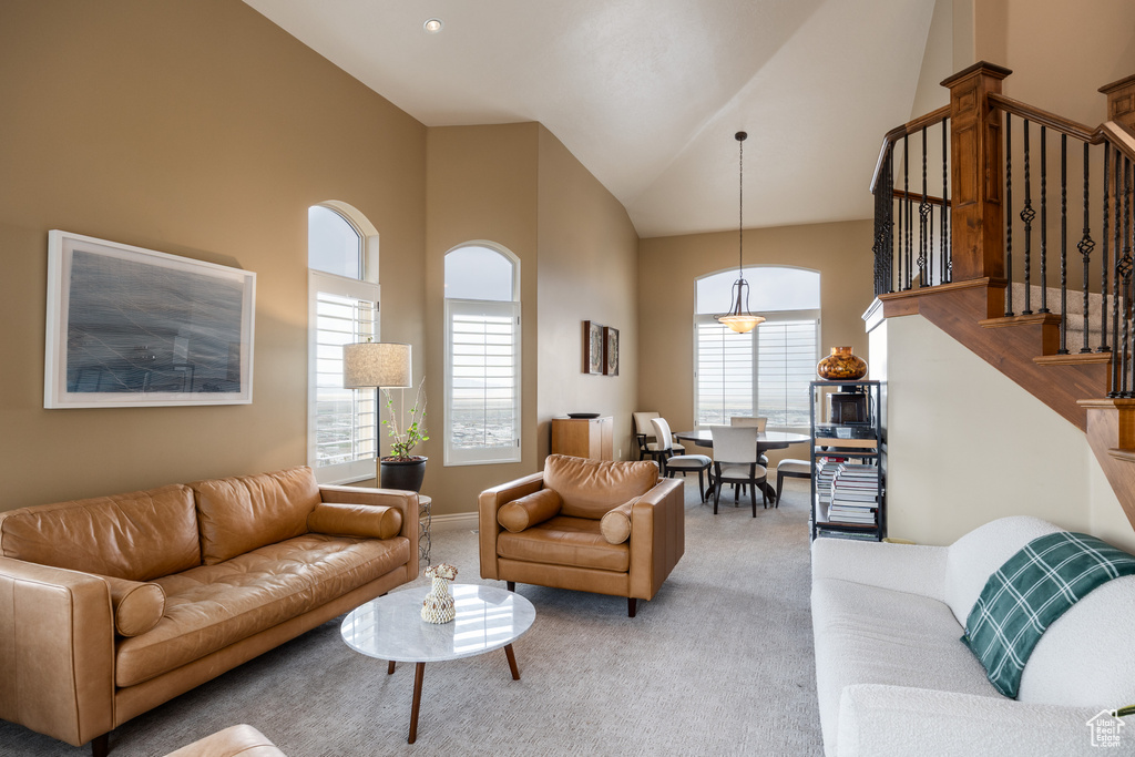 Living room featuring light carpet, stairs, high vaulted ceiling, and baseboards