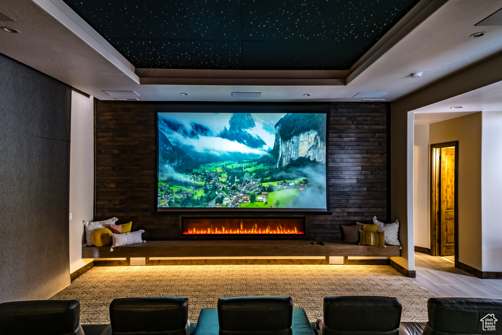Cinema room featuring a lit fireplace, wood finished floors, and a raised ceiling