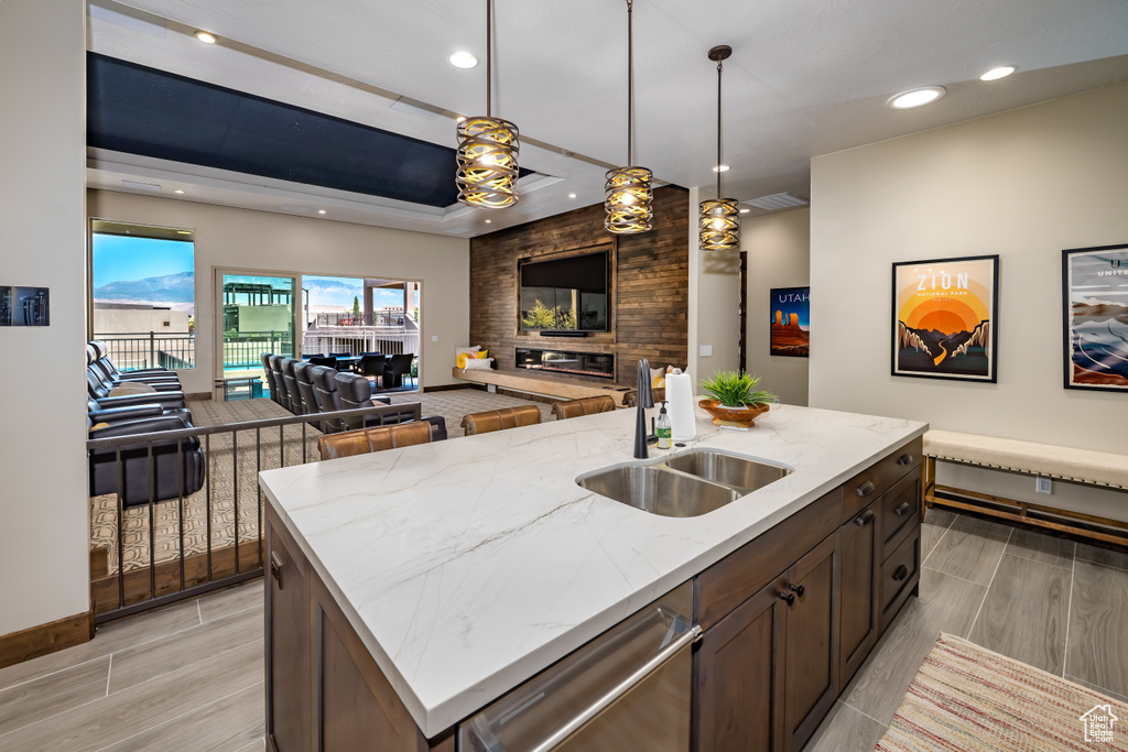 Kitchen with a sink, pendant lighting, open floor plan, stainless steel dishwasher, and light stone countertops