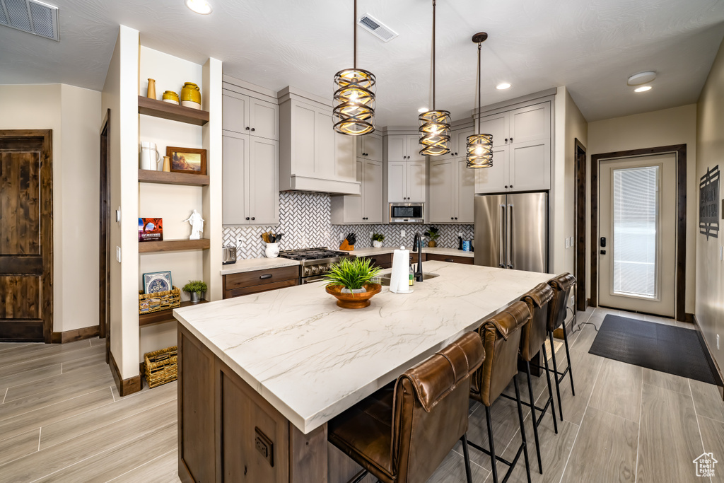 Kitchen featuring high end appliances, open shelves, visible vents, and a sink