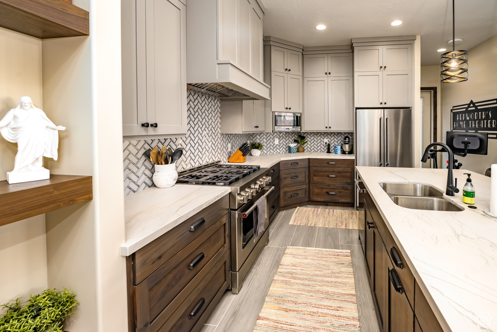 Kitchen featuring a sink, high end appliances, decorative backsplash, light stone counters, and custom exhaust hood