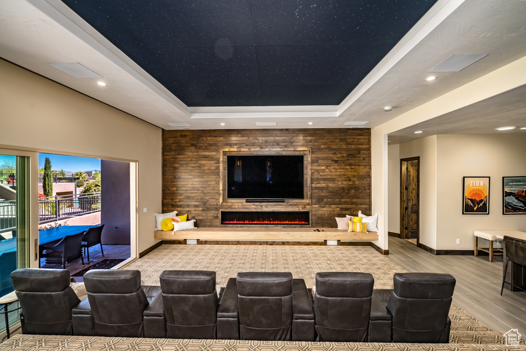 Cinema room featuring a warm lit fireplace, a tray ceiling, recessed lighting, and wood finished floors
