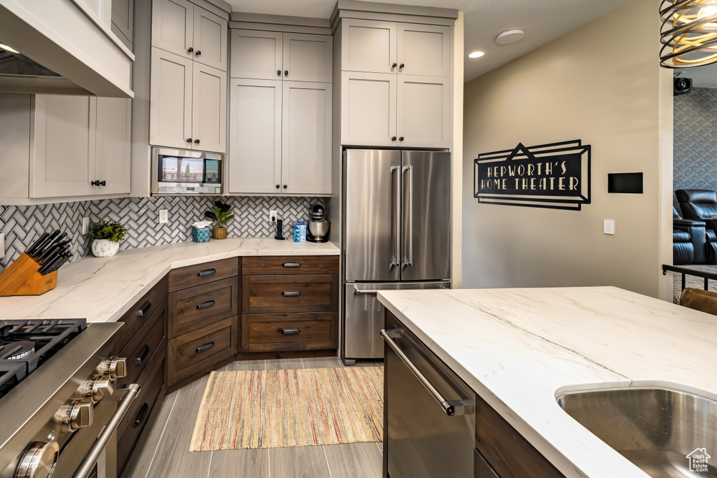 Kitchen featuring light stone countertops, recessed lighting, light wood finished floors, high quality appliances, and tasteful backsplash