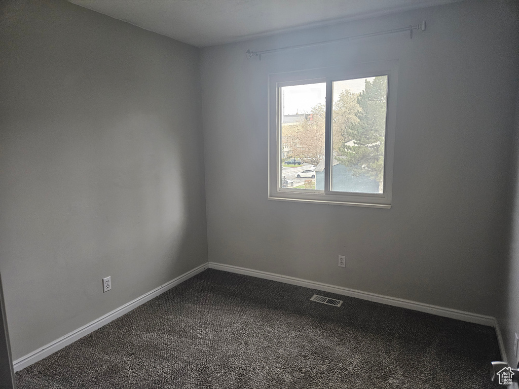 Spare room with baseboards, dark colored carpet, and visible vents