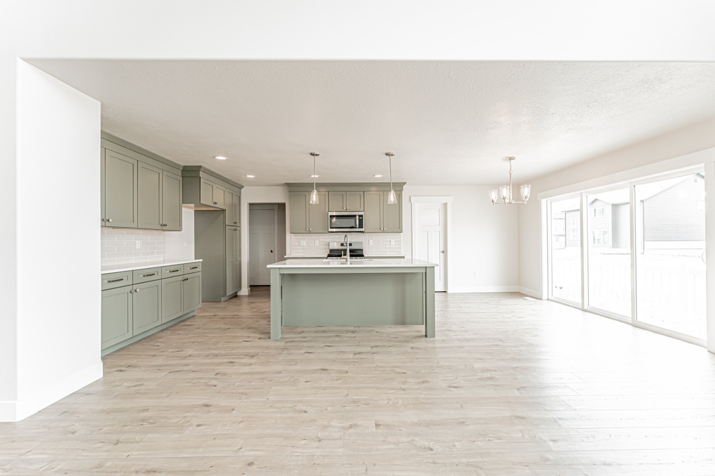Kitchen featuring stainless steel microwave, gray cabinetry, decorative backsplash, a chandelier, and light wood-type flooring