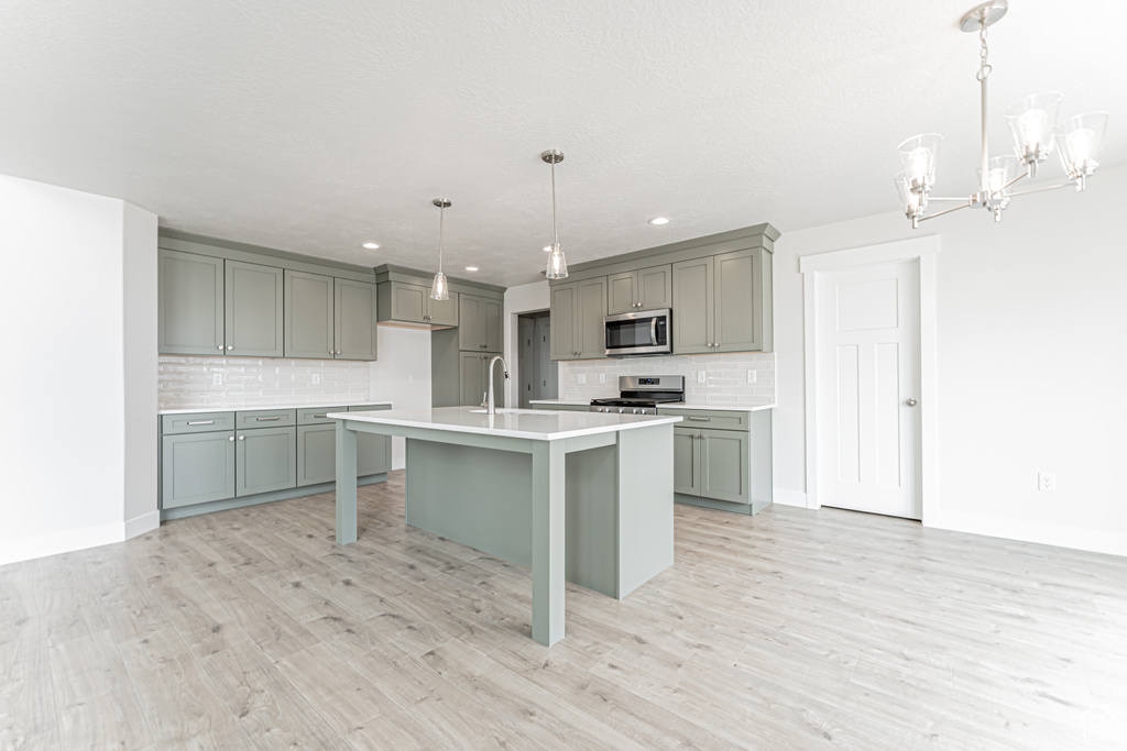 Kitchen with stainless steel appliances, decorative backsplash, a chandelier, gray cabinetry, and recessed lighting