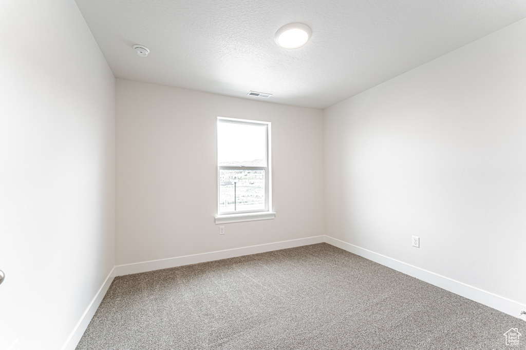 Carpeted spare room with a smoke detector and a textured ceiling