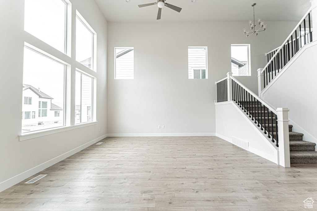 Unfurnished living room featuring plenty of natural light, ceiling fan, stairway, and a chandelier