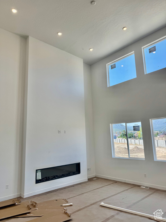 Unfurnished living room featuring plenty of natural light, a glass covered fireplace, recessed lighting, and a high ceiling