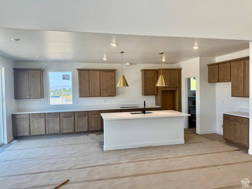 Kitchen featuring an island with sink, hanging light fixtures, a textured ceiling, recessed lighting, and light countertops