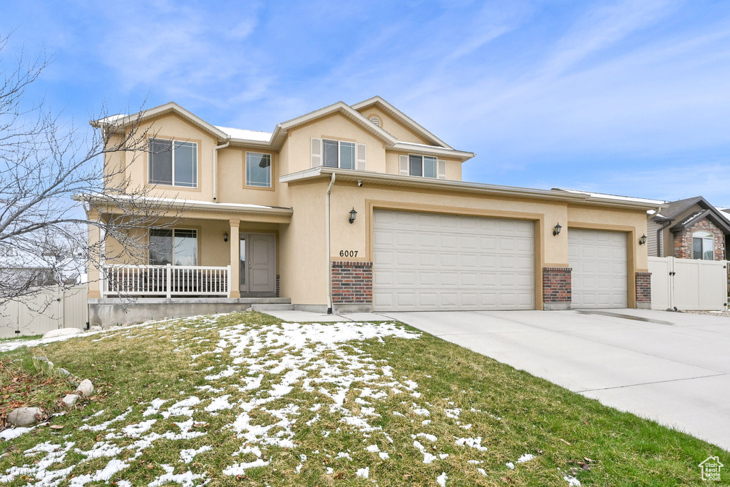 View of front of house featuring driveway, covered porch, stucco siding, fence, and brick siding