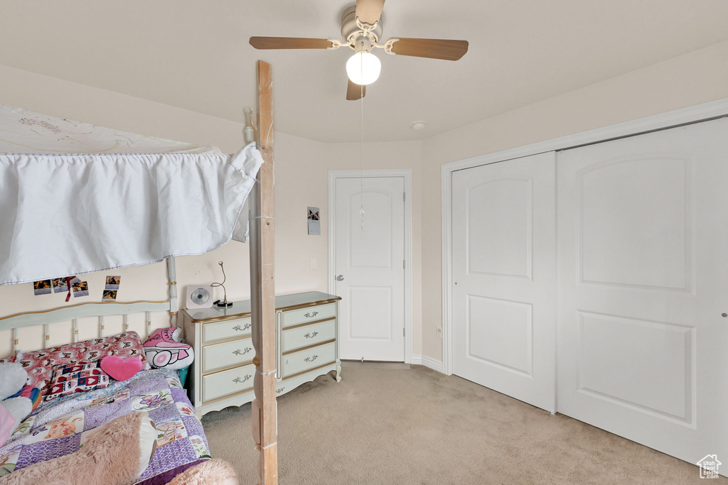 Bedroom with light colored carpet, a closet, and a ceiling fan