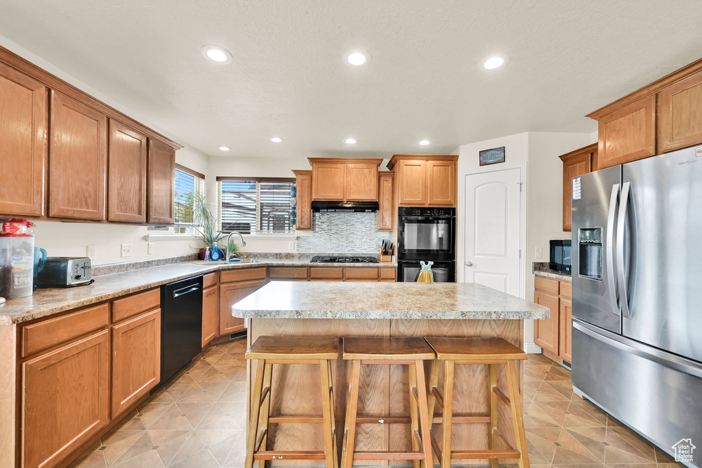 Kitchen featuring a kitchen breakfast bar, a center island, under cabinet range hood, a sink, and black appliances