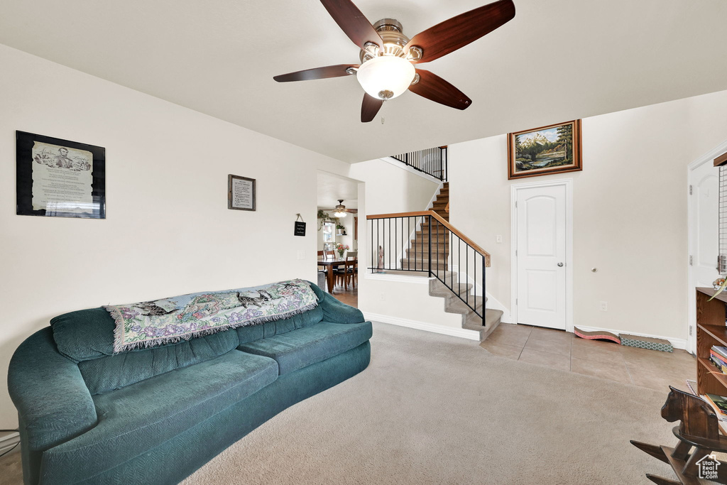 Living room featuring carpet floors, stairway, tile patterned flooring, baseboards, and ceiling fan