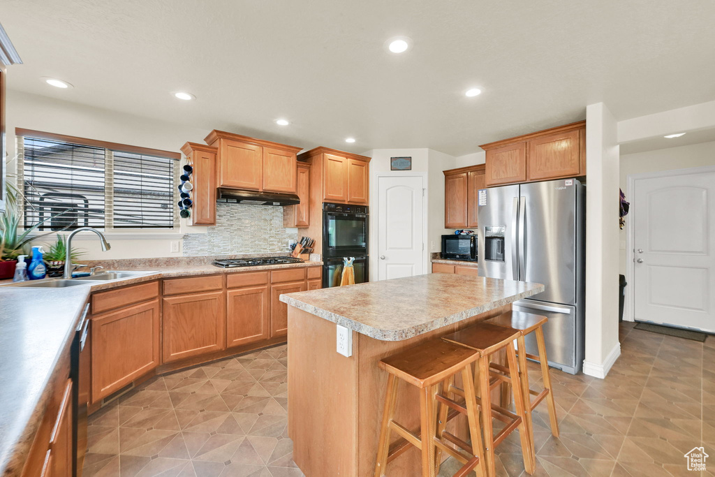 Kitchen featuring light countertops, a kitchen island, under cabinet range hood, a sink, and black appliances