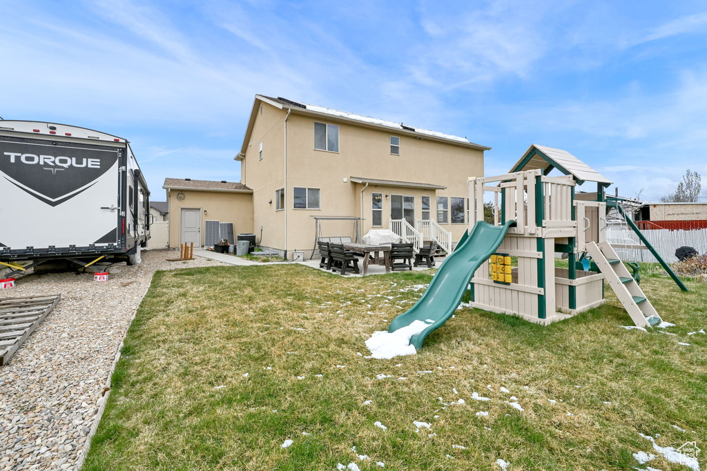 Back of house featuring fence, a playground, stucco siding, cooling unit, and a yard