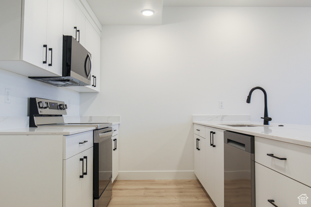 Kitchen with stainless steel appliances, a sink, light wood finished floors, white cabinets, and light stone countertops