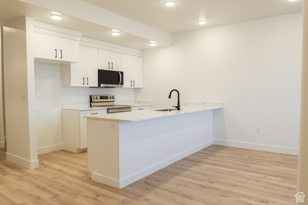 Kitchen with a peninsula, light wood finished floors, stainless steel appliances, white cabinetry, and a sink
