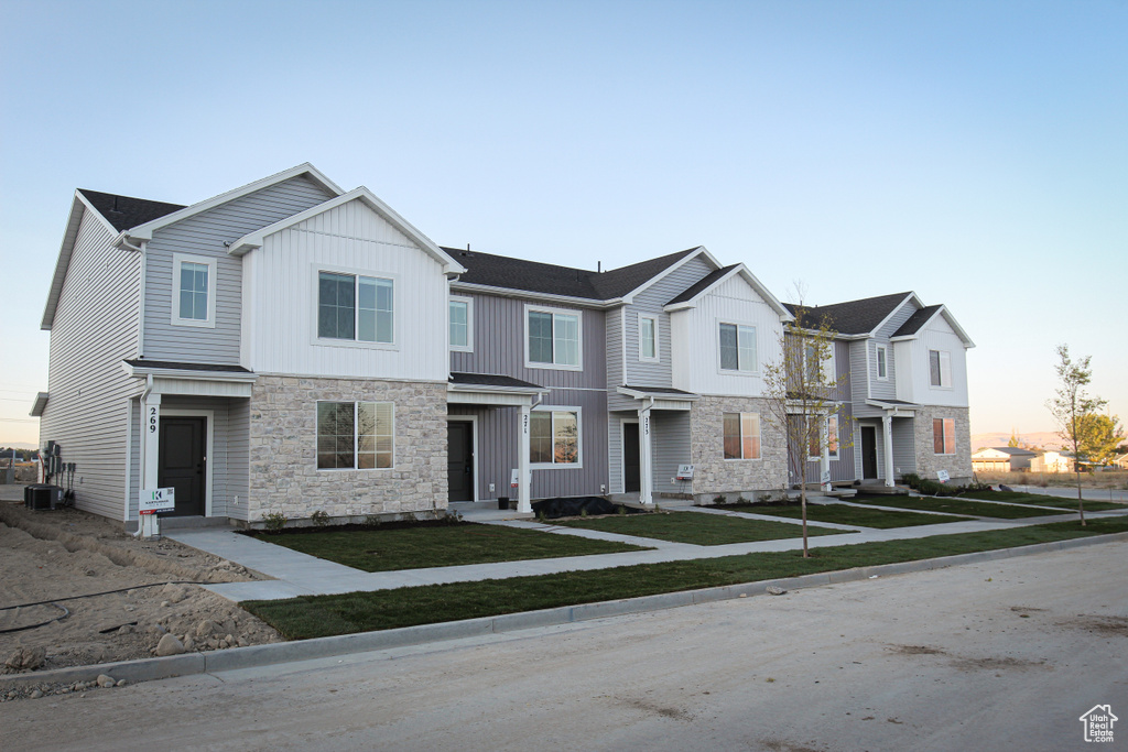 Townhome / multi-family property with cooling unit, stone siding, and a yard