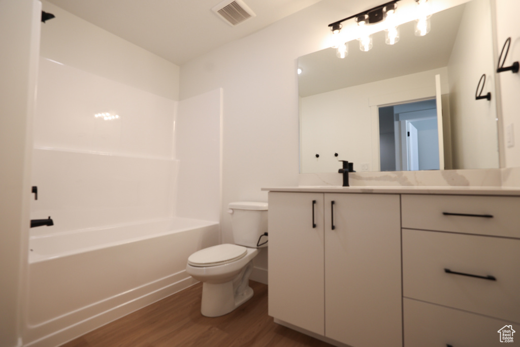 Bathroom featuring vanity, toilet, visible vents, shower / bathtub combination, and wood finished floors