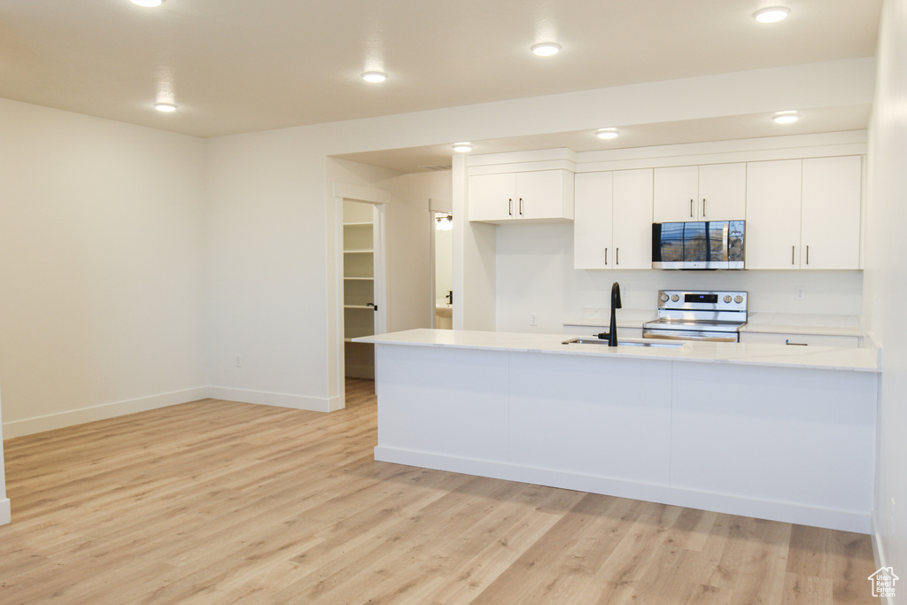 Kitchen with light countertops, light wood-style flooring, appliances with stainless steel finishes, and white cabinets