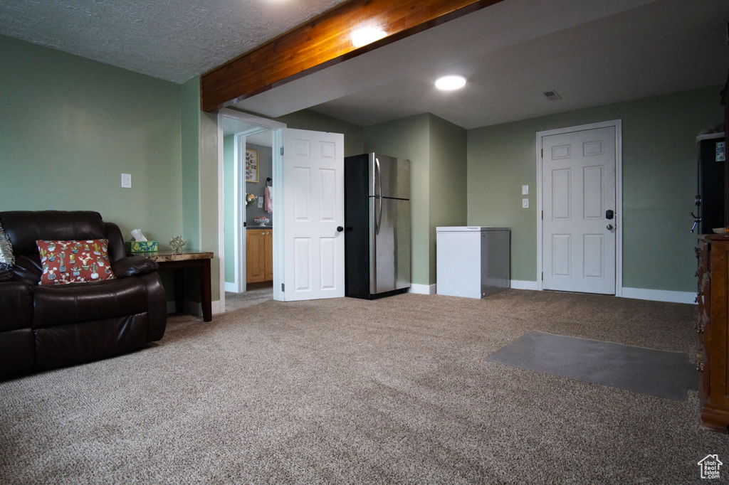 Carpeted living area featuring baseboards, visible vents, and beamed ceiling
