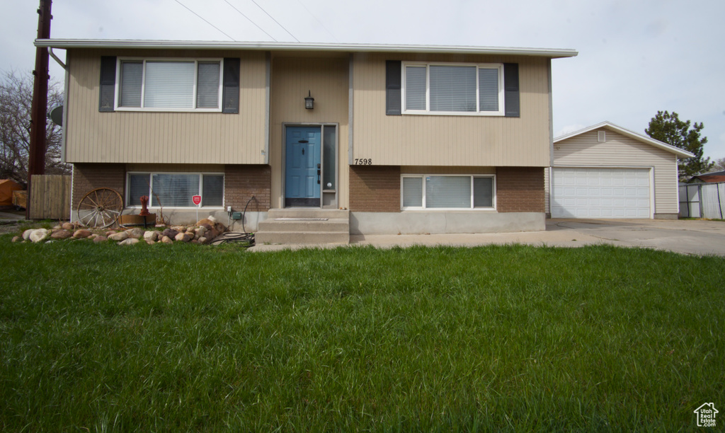 Split foyer home with an outbuilding, concrete driveway, a front yard, brick siding, and a garage