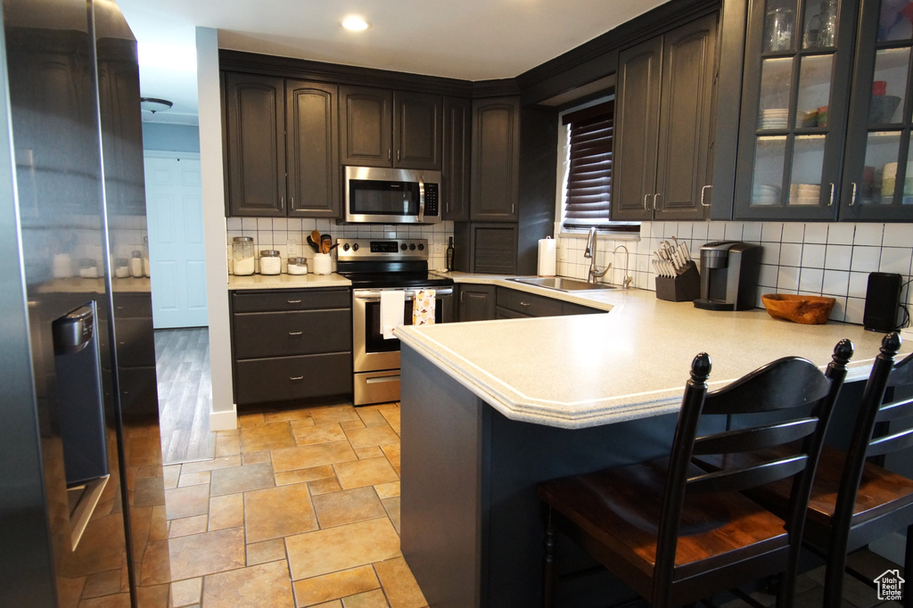 Kitchen with light countertops, a sink, appliances with stainless steel finishes, and a kitchen bar
