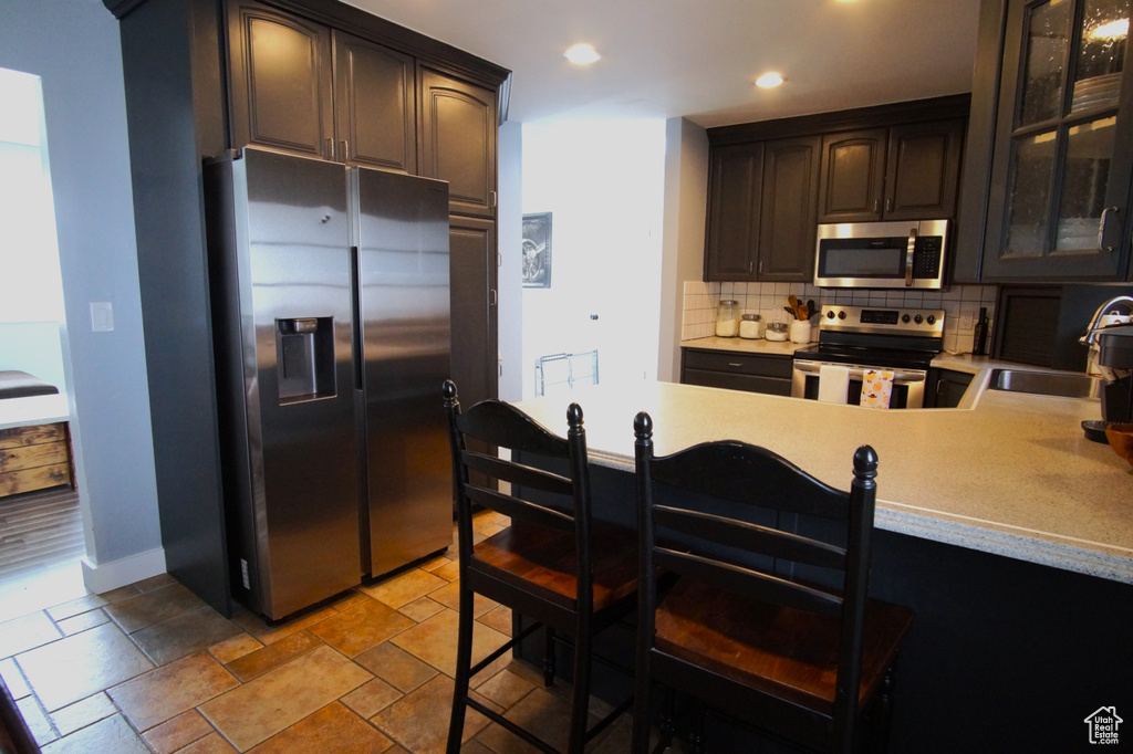 Kitchen with light countertops, a sink, tasteful backsplash, appliances with stainless steel finishes, and glass insert cabinets