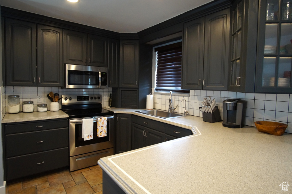 Kitchen with a sink, backsplash, light countertops, and appliances with stainless steel finishes