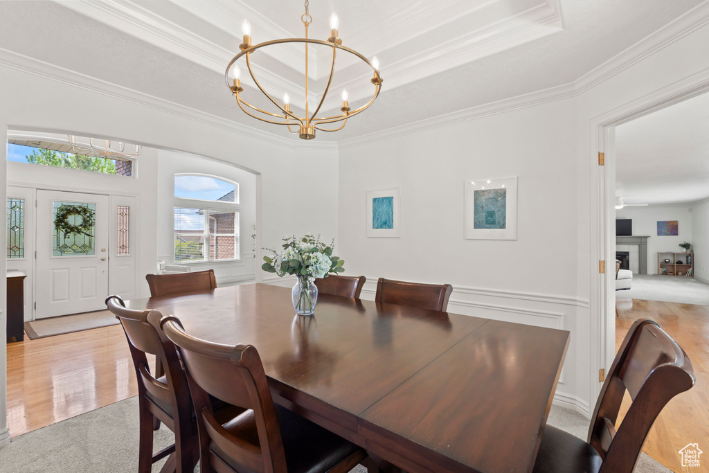 Dining space featuring a chandelier, ornamental molding, light wood finished floors, a raised ceiling, and light carpet