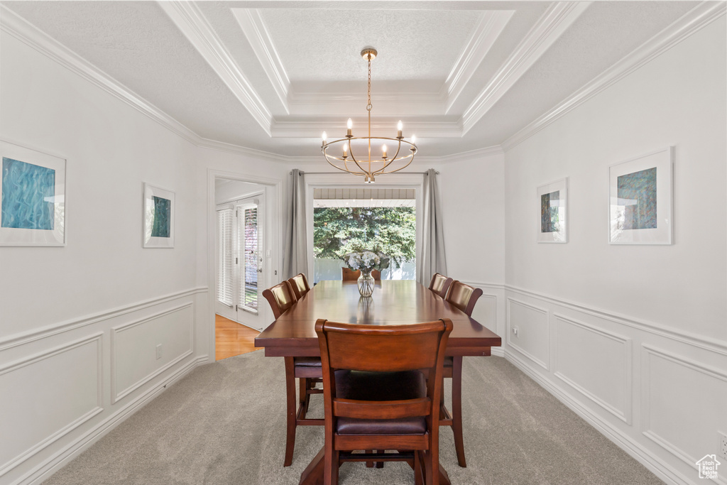Dining room with a tray ceiling, a chandelier, crown molding, light colored carpet, and a decorative wall