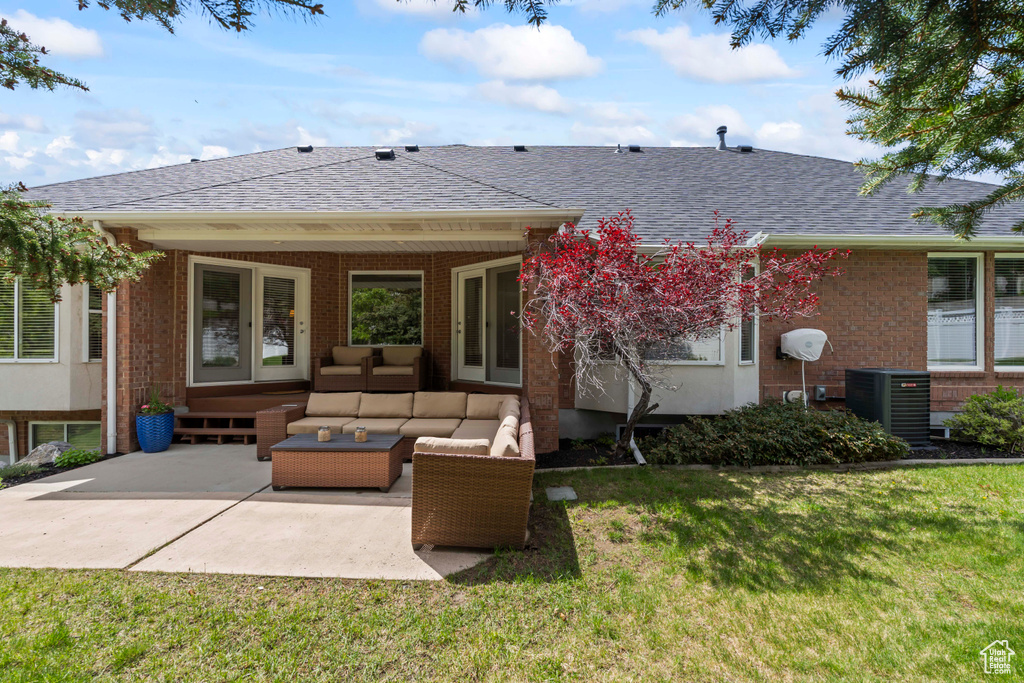 Rear view of house with central air condition unit, outdoor lounge area, a patio, roof with shingles, and a lawn