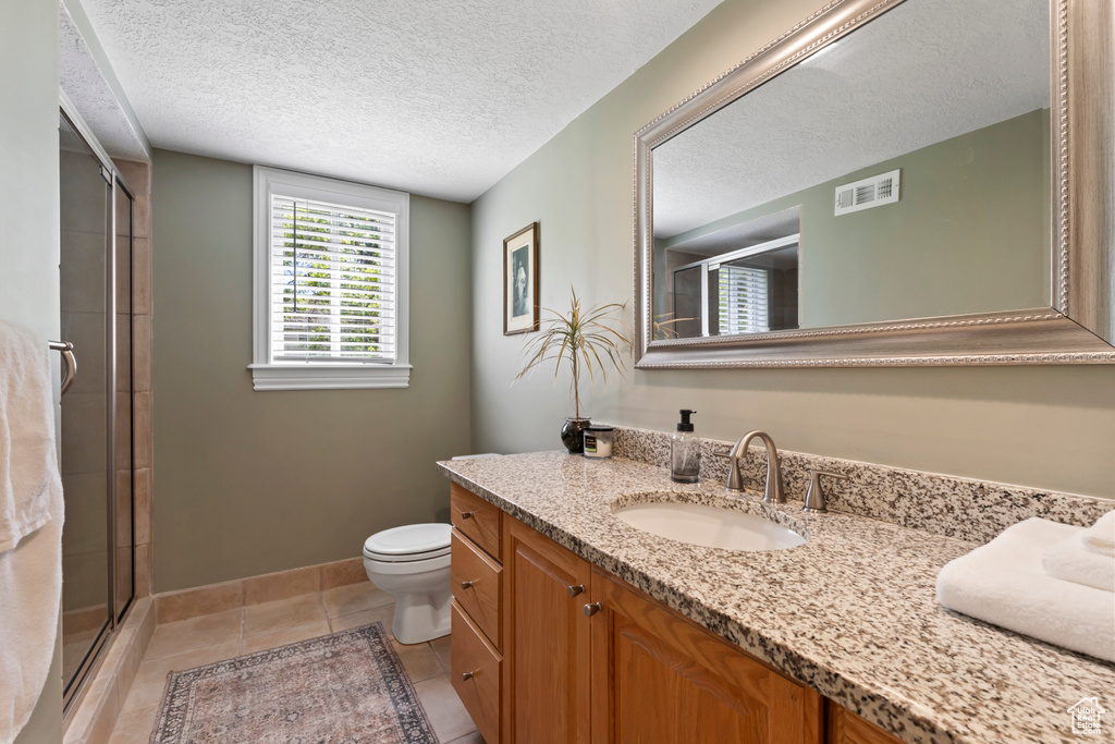 Full bathroom with vanity, an enclosed shower, toilet, a textured ceiling, and tile patterned flooring
