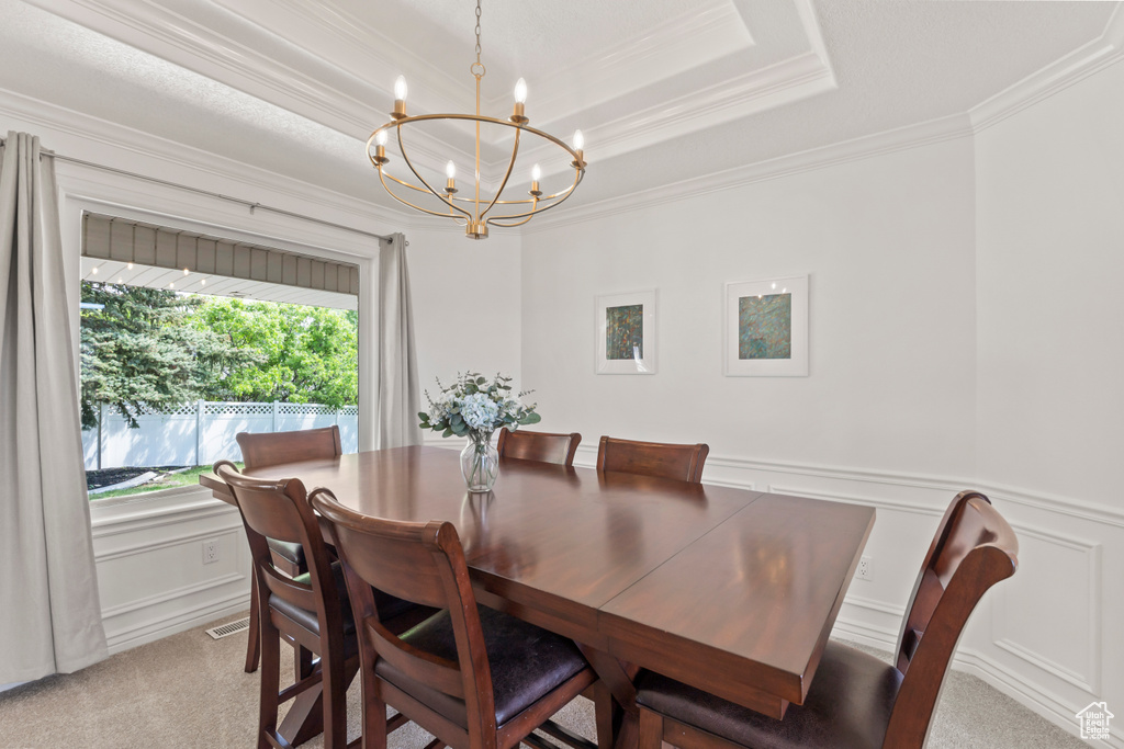 Dining area with a chandelier, ornamental molding, light colored carpet, a decorative wall, and a raised ceiling