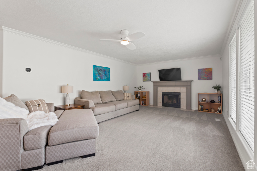 Living area featuring a ceiling fan, crown molding, carpet floors, a tile fireplace, and baseboards