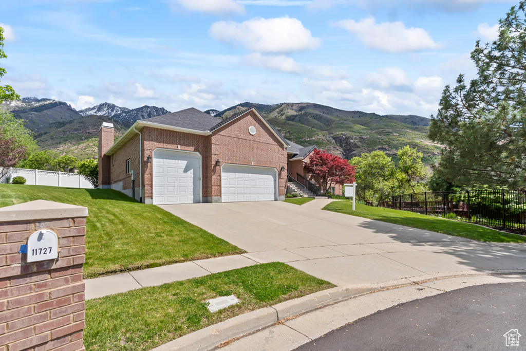 View of front facade with brick siding, an attached garage, a mountain view, concrete driveway, and a chimney