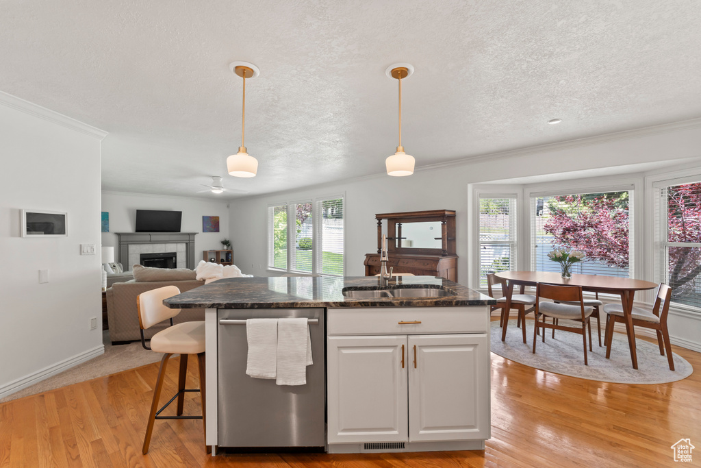 Kitchen with a sink, a textured ceiling, stainless steel dishwasher, a tile fireplace, and decorative light fixtures
