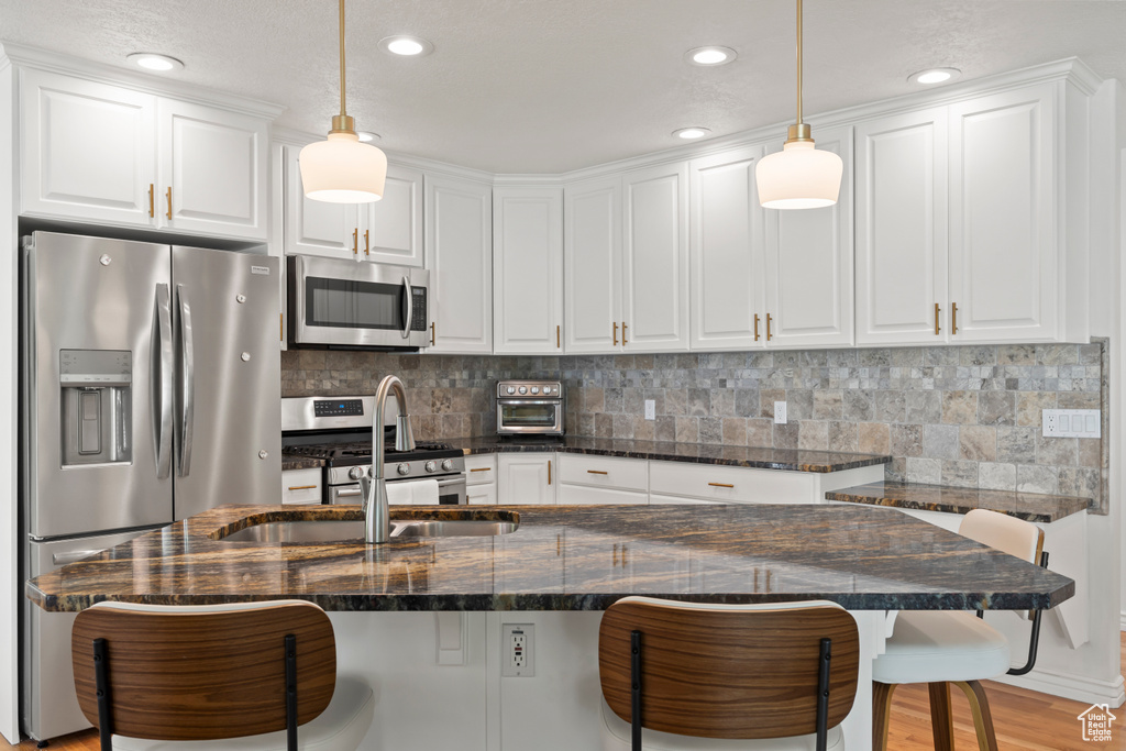 Kitchen with stainless steel appliances, a sink, white cabinets, a kitchen bar, and recessed lighting