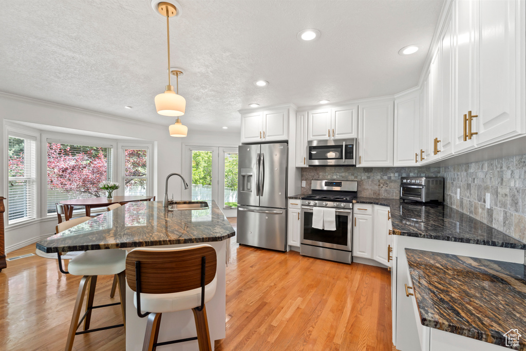 Kitchen featuring appliances with stainless steel finishes, a sink, a breakfast bar area, white cabinetry, and decorative backsplash