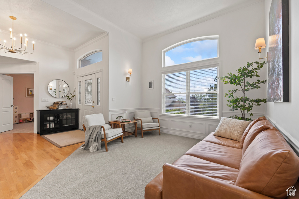 Living area featuring crown molding, a chandelier, a towering ceiling, a wainscoted wall, and light wood-style floors