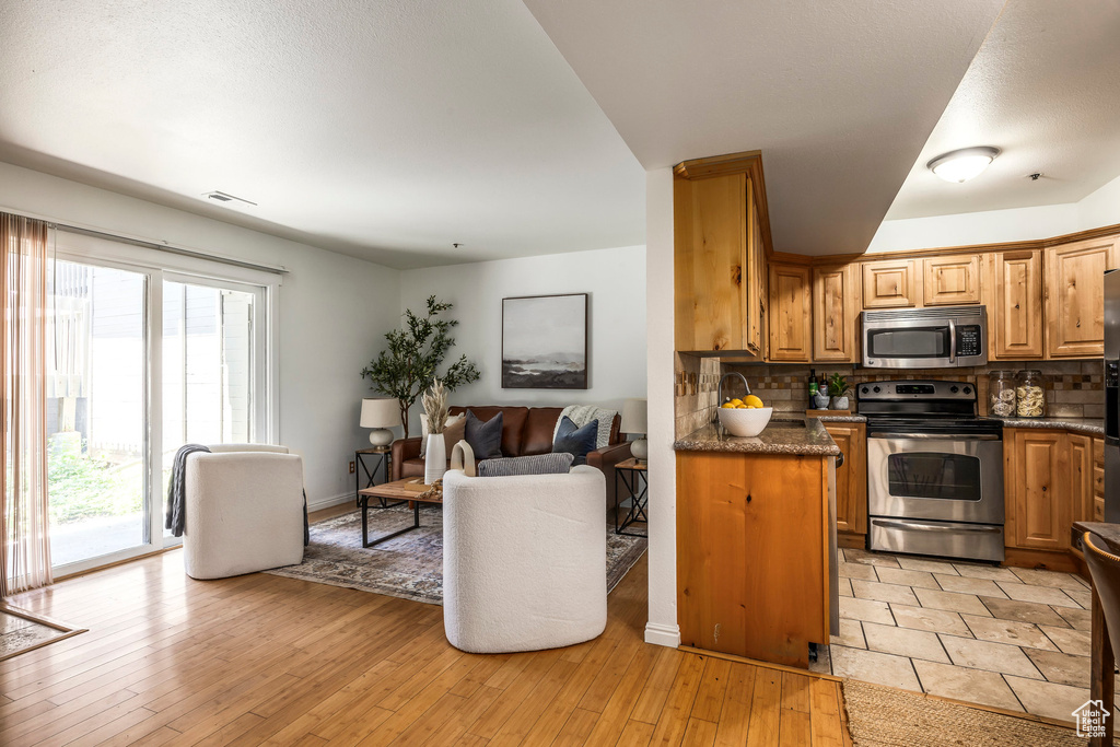Kitchen with stainless steel appliances, tasteful backsplash, open floor plan, light wood-style floors, and brown cabinetry