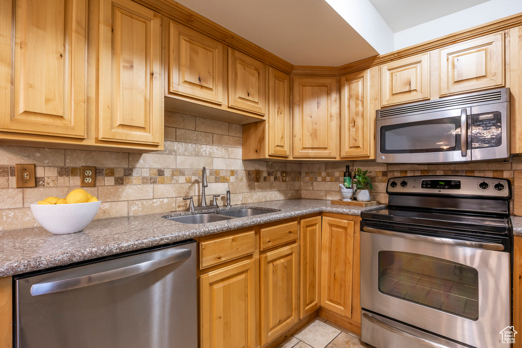Kitchen with appliances with stainless steel finishes, backsplash, light tile patterned flooring, and stone countertops