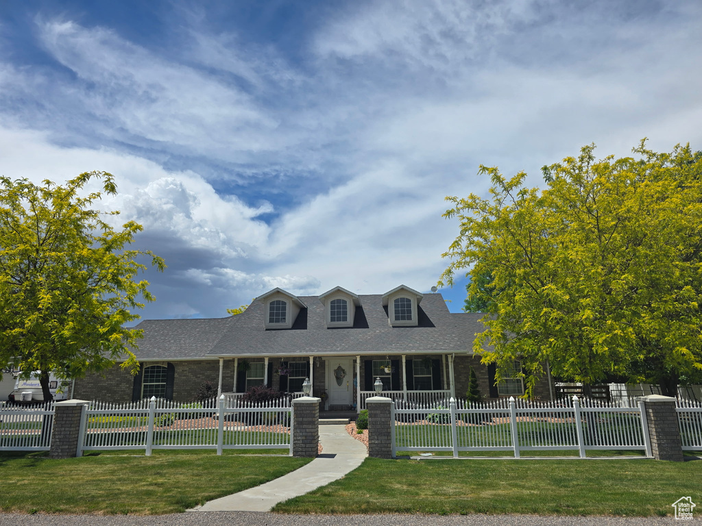 Cape cod home with a shingled roof, brick siding, and covered porch