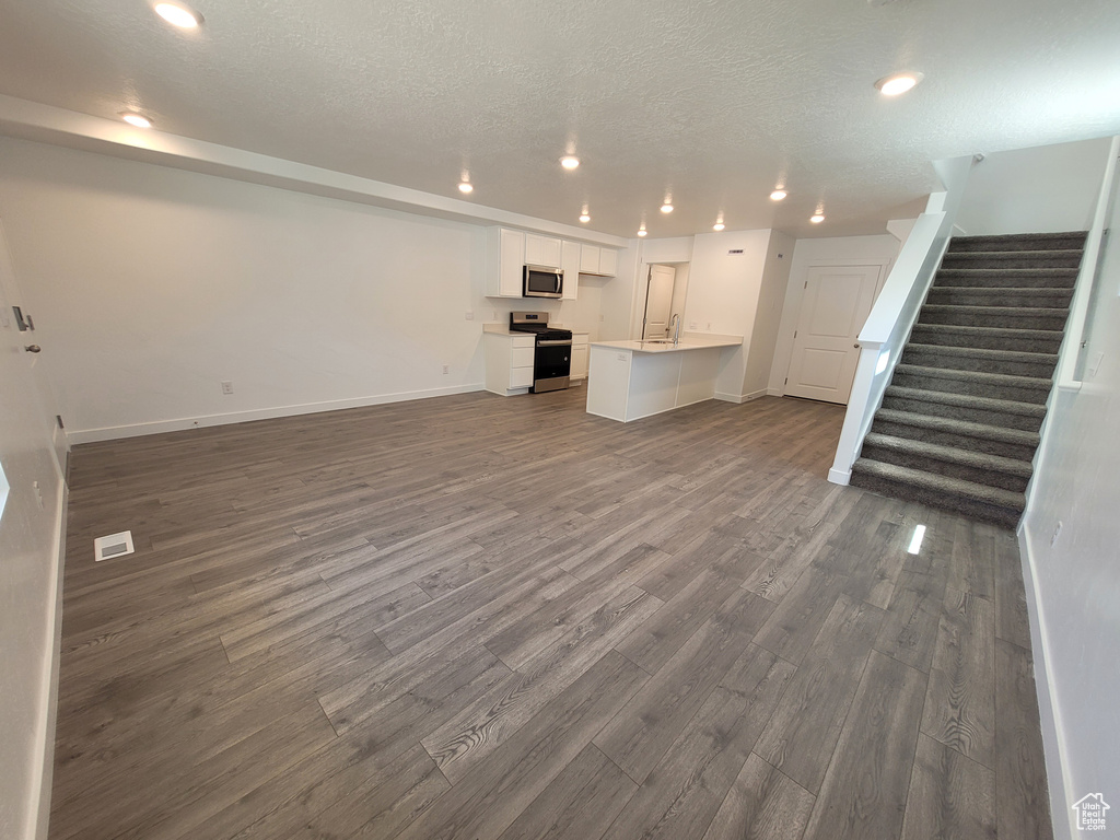 Unfurnished living room featuring dark wood-type flooring, stairs, recessed lighting, and a textured ceiling