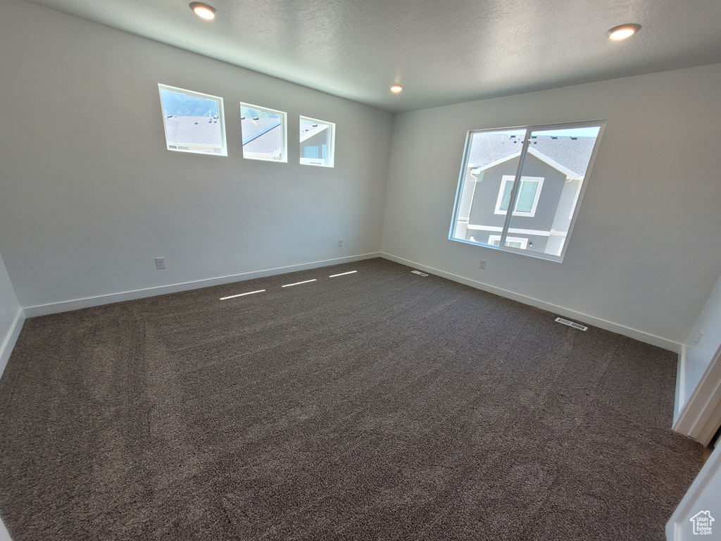 Spare room featuring healthy amount of natural light, dark carpet, and recessed lighting